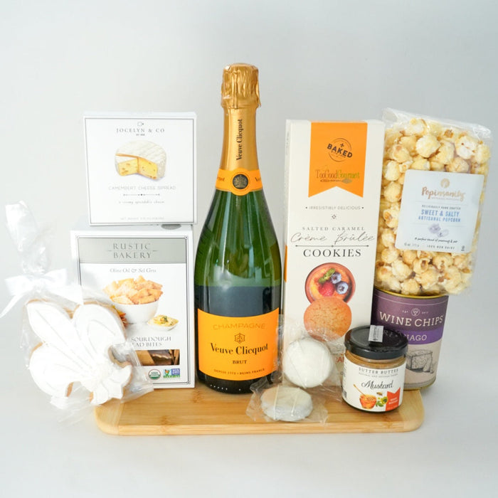 Bottle of champagne, popcorn, cookies, and other snacks on a wooden tray with a white background