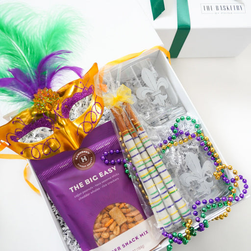 Gift box with snacks, a mask, and festive decorations on a white surface.