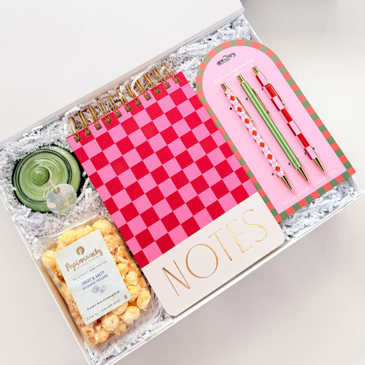 Gift box with stationery items including a notebook, pen, and snacks on a white background