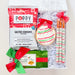 A curated holiday gift box filled with treats, including a bag of Poppy Salted Caramel Popcorn, a decorated cookie with red and green icing, two wrapped candy canes, and a box of chocolate chip cookies, all arranged in white crinkle paper inside an open white box.
