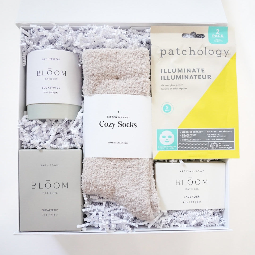 Gift set with 'Bloom' candle, 'Cozy Socks', and 'Patchology' product in a box on a white background