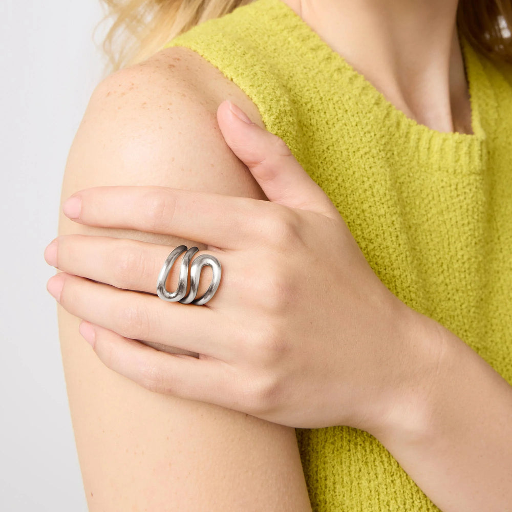 Studio photograph of a sculptural silver ring with a triple wavy band design worn on a hand resting against a lime green textured knit top and freckled shoulder