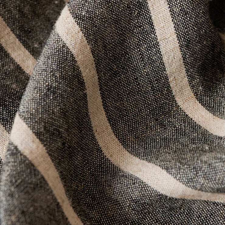 Woven linen textile close-up showcasing thick cream stripes across a speckled charcoal black background with visible natural fiber slubs and soft draped ripples