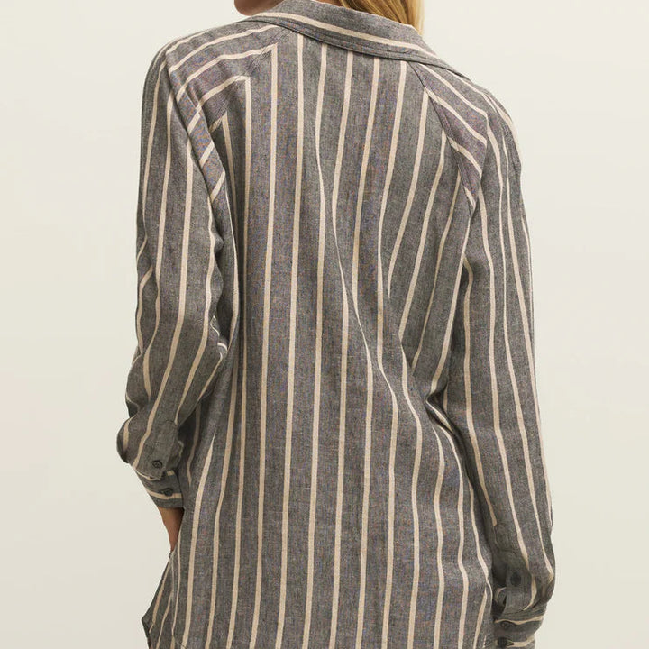 Photograph of a woman from the back wearing a charcoal and beige vertical striped linen shirt featuring raglan sleeves and button-fastening cuffs against a plain studio background
