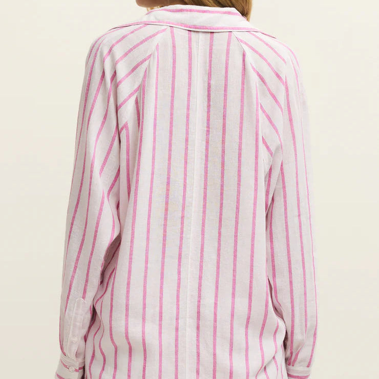 Studio photograph of a woman from the back in a studio setting wearing a white shirt with vibrant pink vertical stripes, textured fabric, and buttoned cuffs