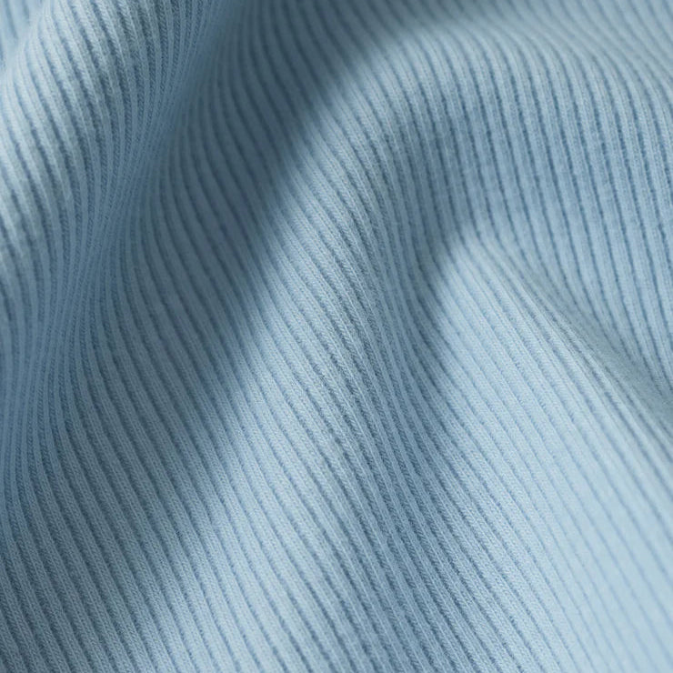 Macro photograph of light blue ribbed fabric featuring distinct vertical textures, soft draped folds, and a cool powder blue hue