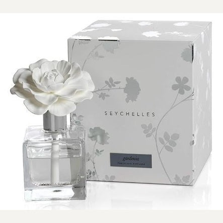 Porcelain air diffuser by The White Company featuring a blooming white ceramic gardenia topper and clear square glass bottle displayed next to a silver floral-patterned Seychelles gift box