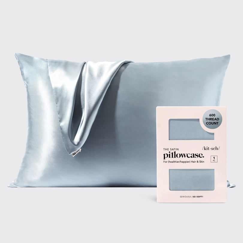 Studio photograph by Kitsch of an ice blue satin pillowcase and its 600 thread count retail packaging featuring shimmering draped fabric and a smooth lustrous finish against a neutral studio background