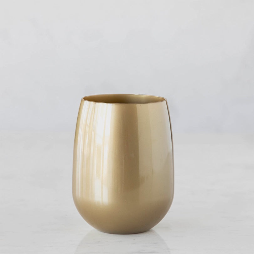 Photograph of a metallic gold stemless wine glass centered on a white marble surface featuring a smooth reflective finish and a modern rounded silhouette