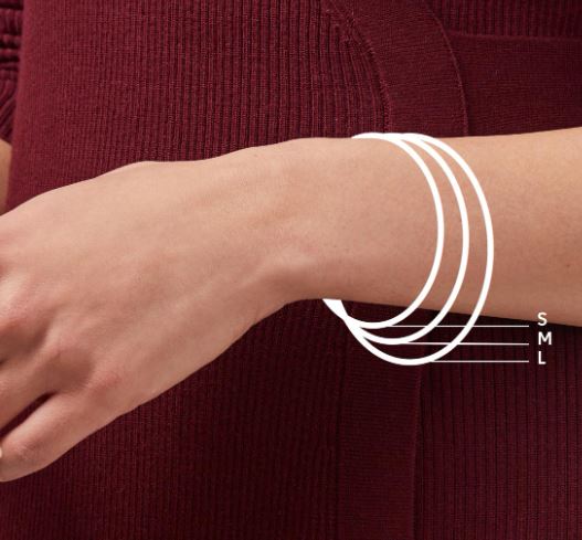 Digital photograph of a jewelry sizing guide on a wrist showing three white concentric circles labeled S M and L against a textured maroon ribbed sweater background
