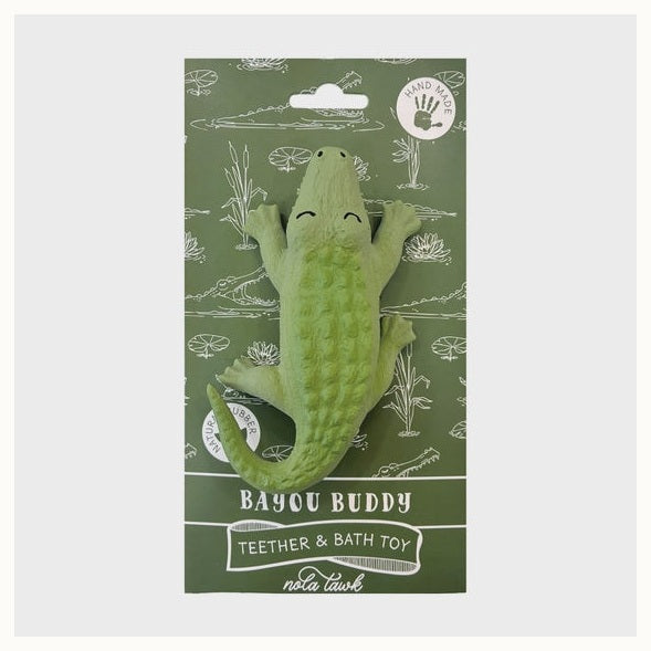 Natural rubber teether by Nola Tawk featuring a light green alligator toy on a Bayou Buddy packaging card representing the Louisiana bayou with white swamp plant illustrations, a bumpy textured skin, and a curved tail