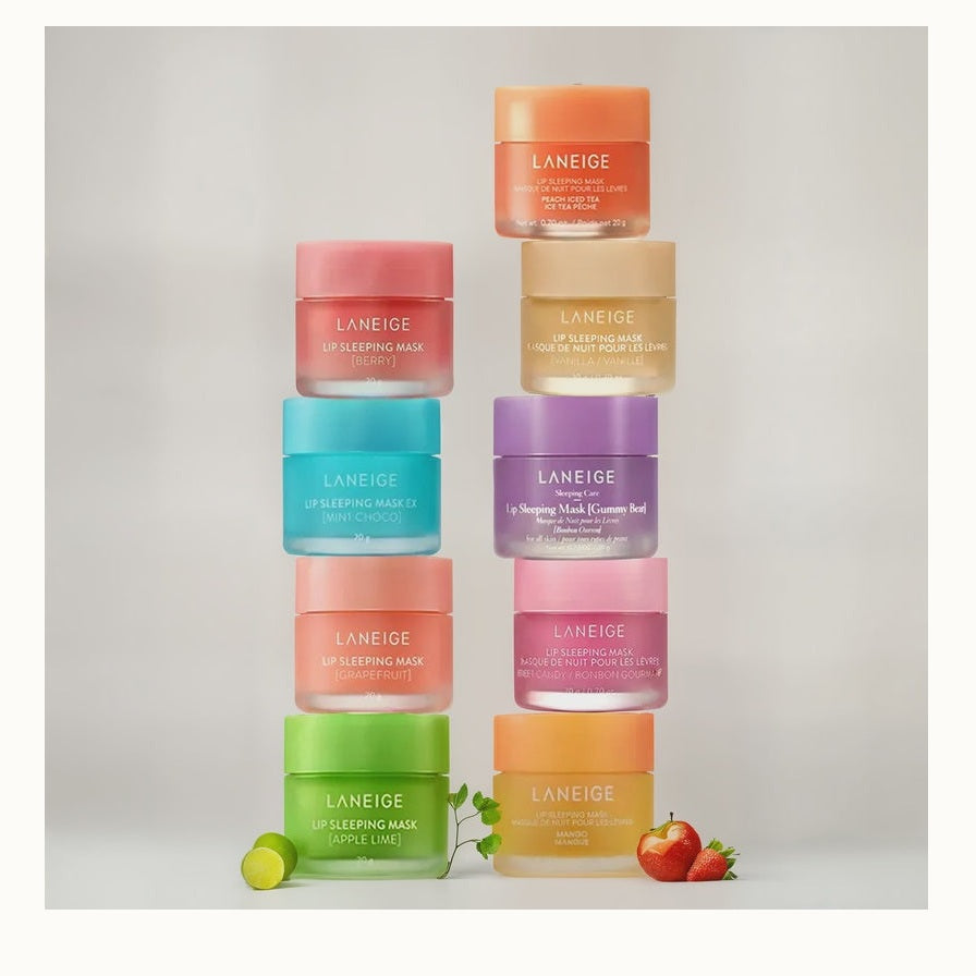 Professional product photograph for Laneige featuring two vertical stacks of Lip Sleeping Mask jars in a studio setting with the prominent Laneige logo, vibrant matte pastel containers in shades of pink and purple, and fresh lime and strawberries at the base