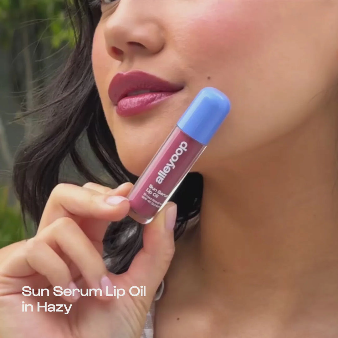 Woman holding an Alleyoop lip oil by her face, with text "Sun Serum Lip Oil in Hazy"