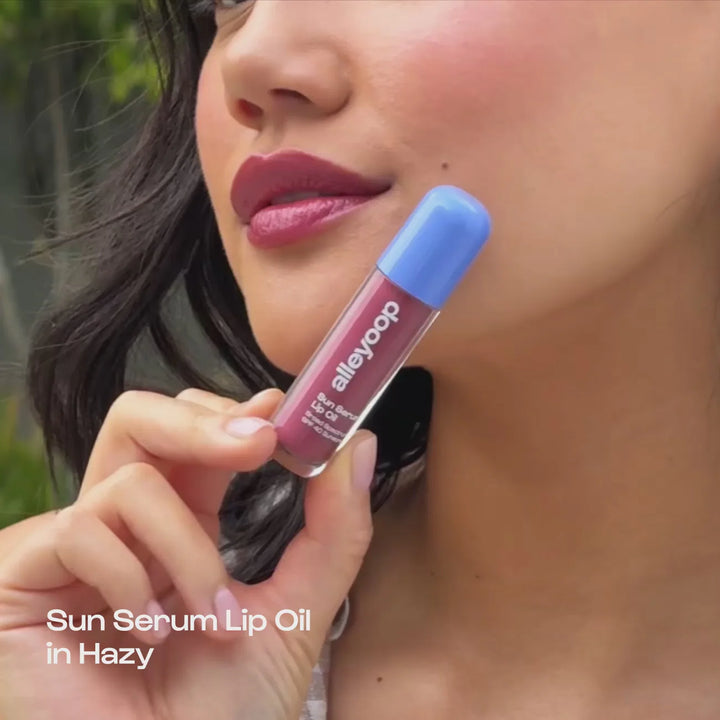 Woman holding an Alleyoop lip oil by her face, with text "Sun Serum Lip Oil in Hazy"