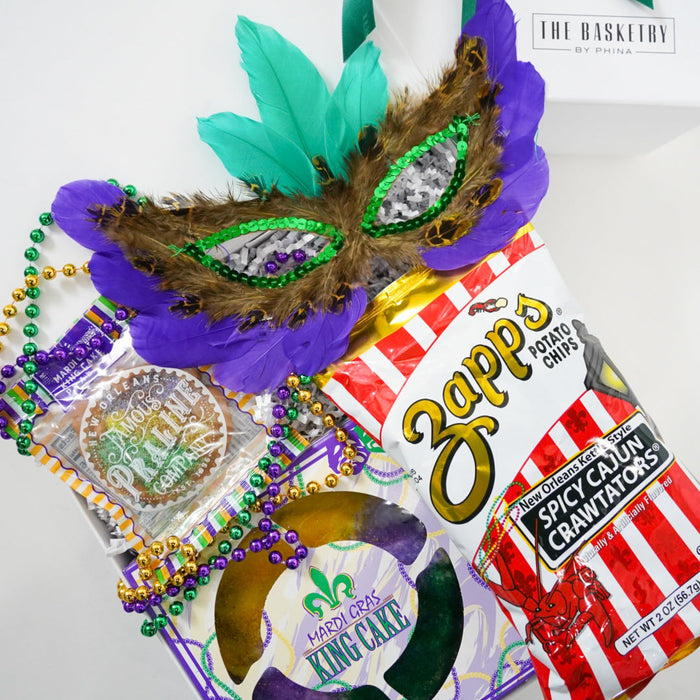 Mardi Gras-themed gift bag with Zippo chips, king cake, and mask on a white background