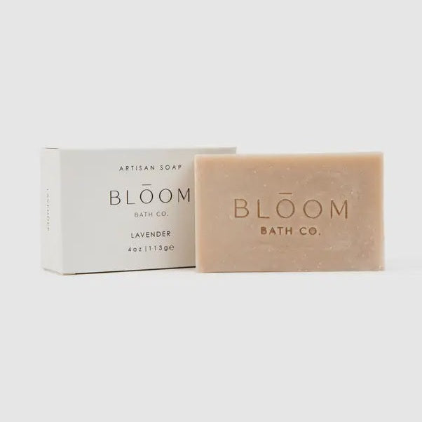 Product photograph by Bloom Bath Co. featuring a lavender artisan soap bar and its white packaging box on a neutral studio background with an embossed brand logo on the textured tan soap and minimalist black serif typography