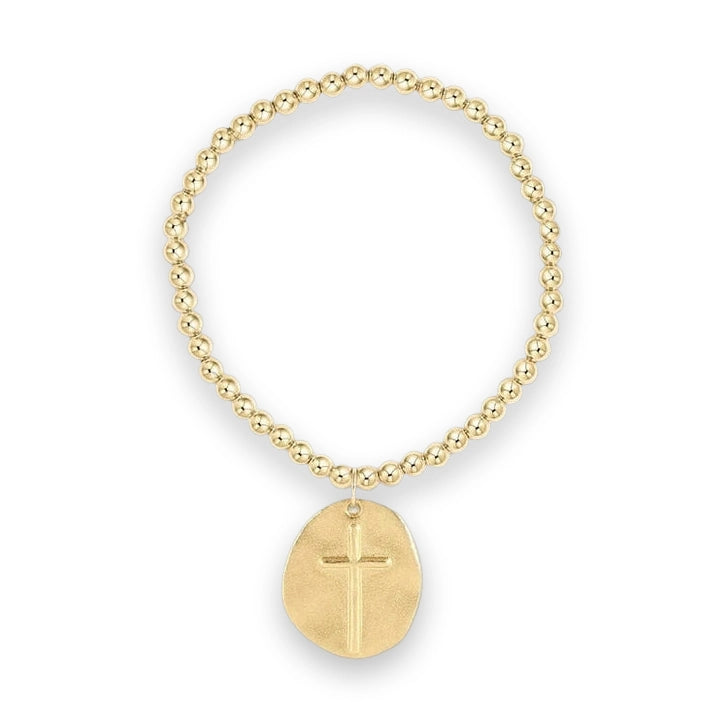 Gold-toned metal beaded jewelry bracelet featuring polished spherical beads and an irregular brushed-metal oval charm with an embossed religious cross symbol centered on a white studio background