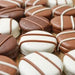 Photograph of gourmet chocolate-covered cookies on a wooden tabletop, showcasing smooth white and milk chocolate coatings accented with elegant parallel drizzle patterns in contrasting tones