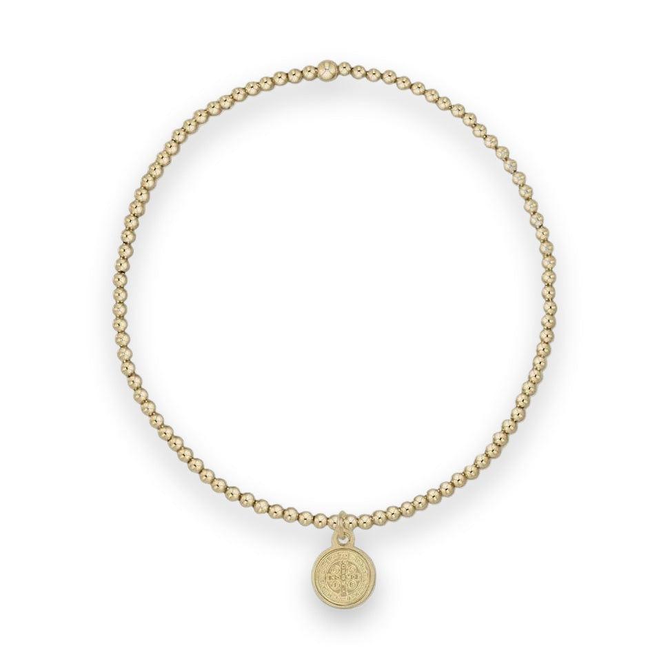 Gold-tone beaded stretch bracelet featuring small polished spherical beads, a single larger accent bead, and an iconic St. Benedict religious medallion pendant centered on a light grey background