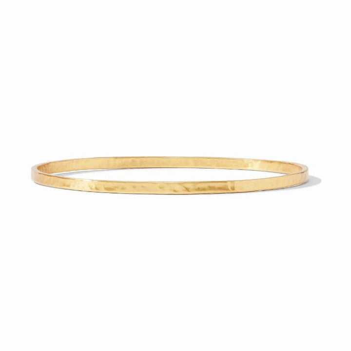 Hammered 18k gold-plated brass jewelry showcasing a minimalist thin bangle bracelet on a white studio background with a textured hand-finished surface and a reflective golden luster
