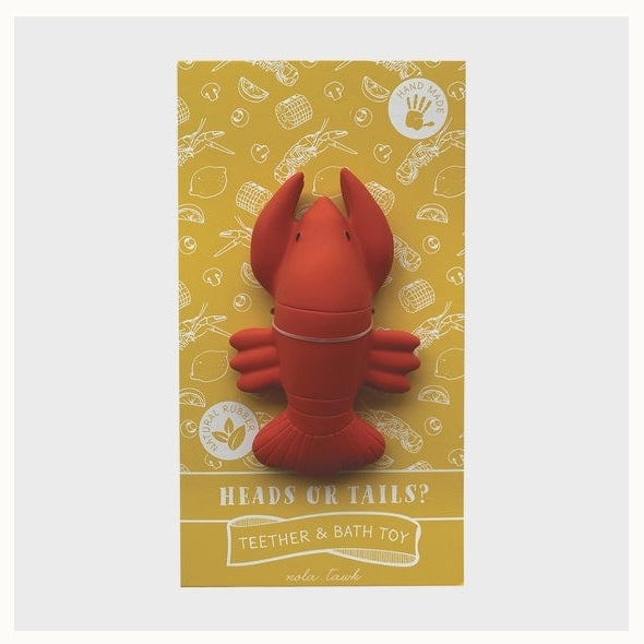 Natural rubber crawfish teether by nola tawk featuring a bright red toy centered on yellow packaging decorated with white line art of lemons and corn and the bold title Heads or Tails