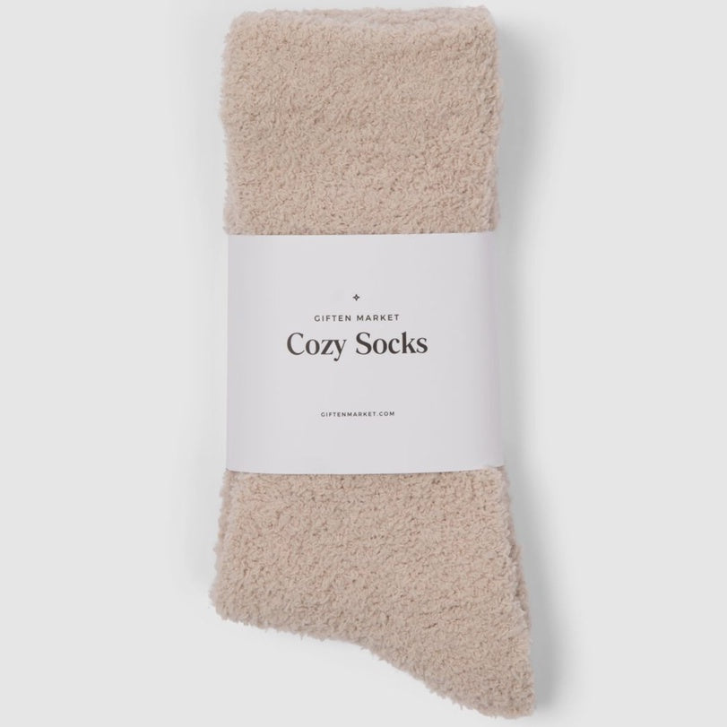 Product photograph by Giften Market of fuzzy beige socks on a light gray background featuring a plush textured surface and a white paper band with the words Cozy Socks in black serif font