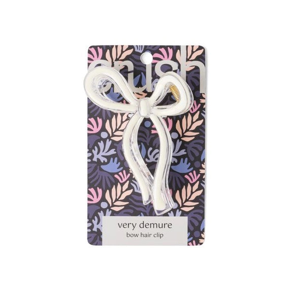 Product photography by Snish featuring a white and clear acrylic bow hair clip centered on a pink and purple leaf patterned retail card with a gold metal spring and the text very demure bow hair clip