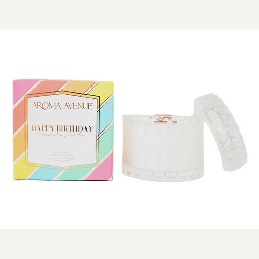 Product photograph by Aroma Avenue of a Happy Birthday Amber Vanilla candle in an iridescent textured glass jar alongside its colorful pastel-striped gift box featuring elegant gold foil borders and lettering