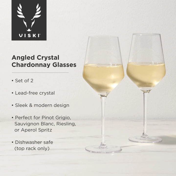 Product photography by Viski of two angled crystal chardonnay glasses filled with pale golden wine on a marble countertop featuring sharp geometric bowls and slender stems beside a black stag head logo