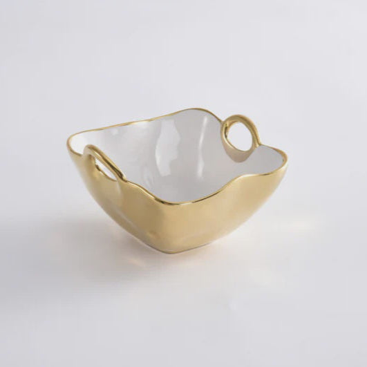 Porcelain serving bowl by Pampa Bay featuring a shimmering gold metallic exterior, a smooth white interior, and organic wavy edges with two integrated ring handles set against a plain white background