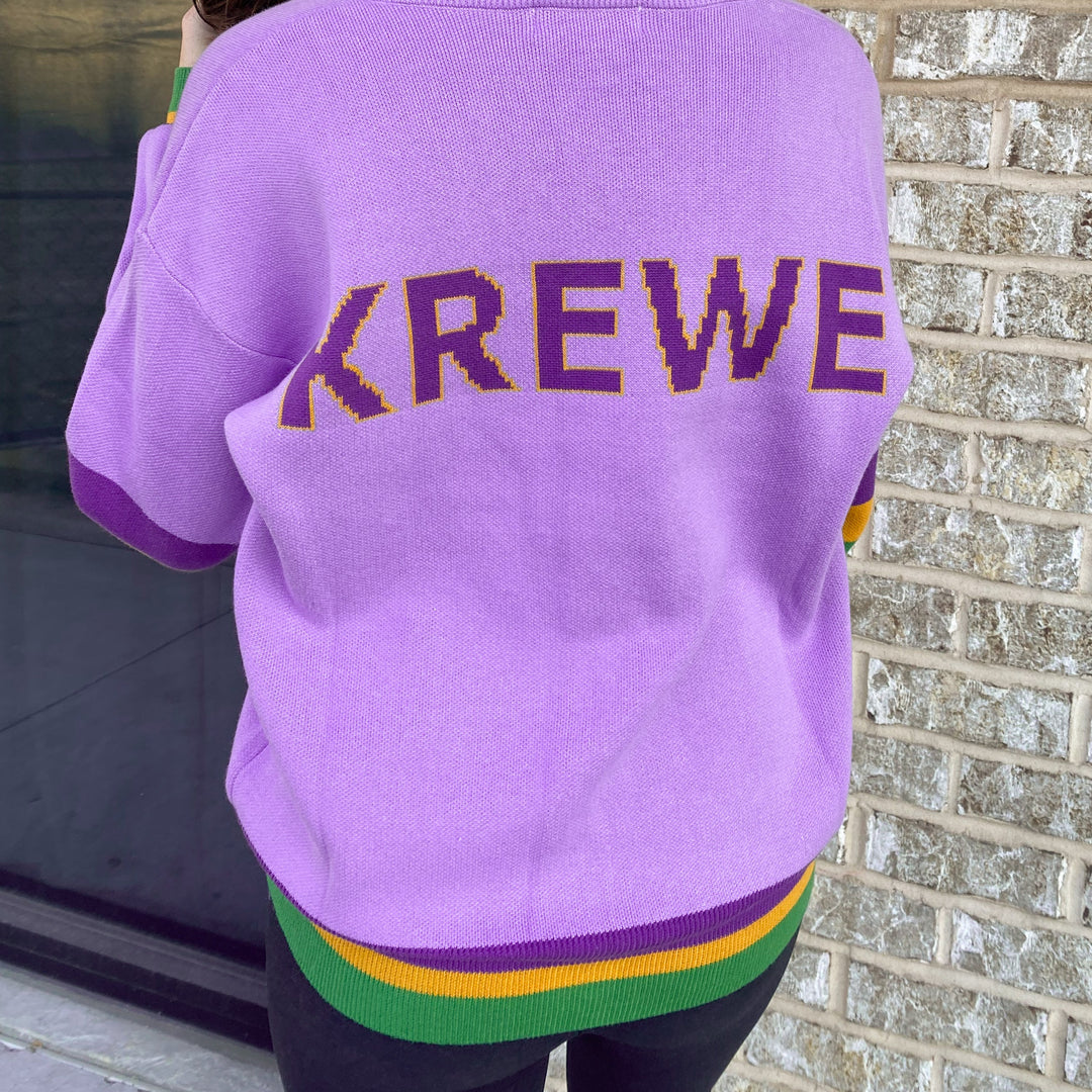 Back of a lavender cardigan with KREWE in purple letters and a purple, green and gold striped hem
