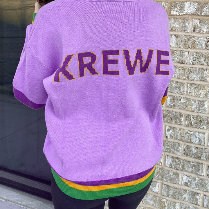 Back of a lavender cardigan with KREWE in purple letters and a purple, green and gold striped hem