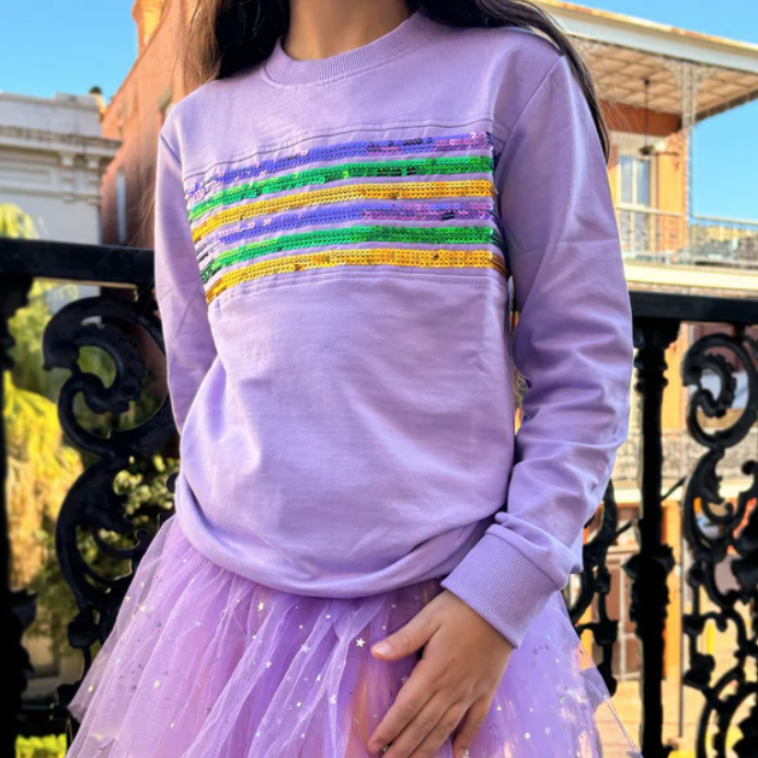 Child in a lavender sweatshirt with purple, green and gold sequin stripes and a purple tulle skirt on a balcony