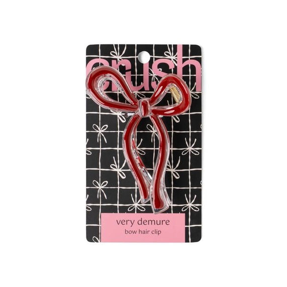 Product photograph by Crush of a red and clear acrylic bow hair clip displayed on a black and white grid patterned card with a pink very demure banner and a small gold spring visible