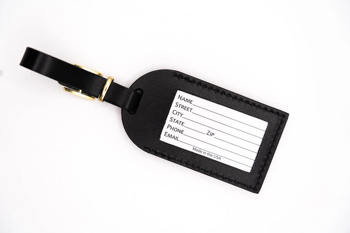Handcrafted black leather luggage tag on a white background featuring a polished gold-toned buckle, precise perimeter stitching, and a white identification card with a Made in the USA label