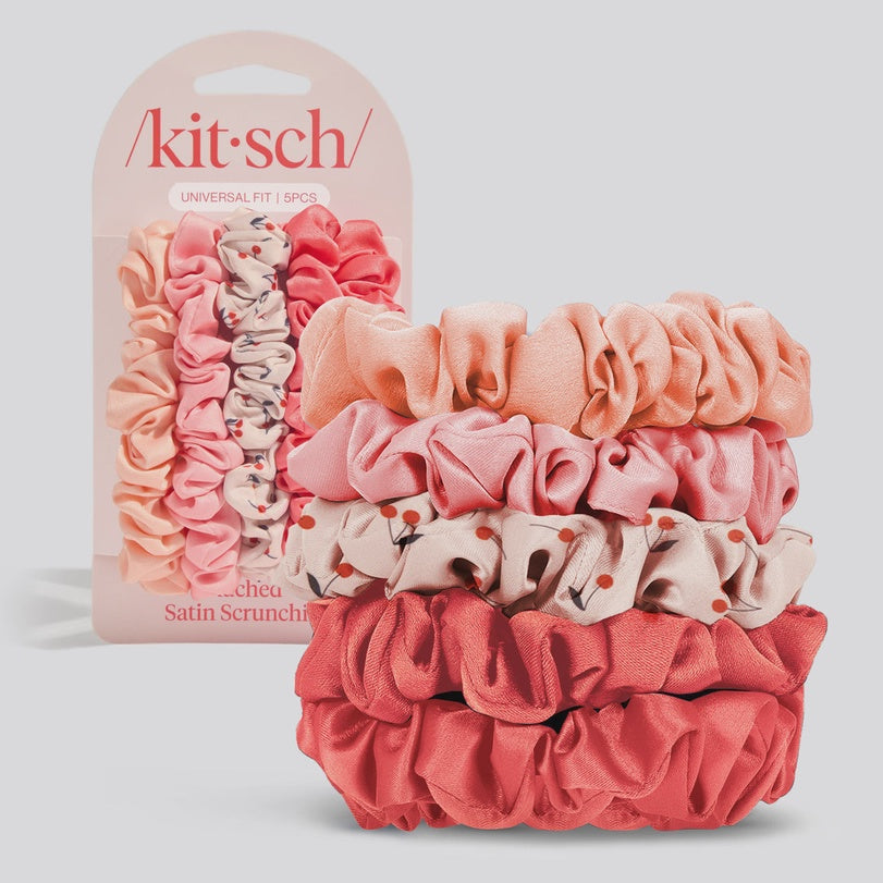 Product photography by Kitsch of a five-piece satin scrunchie set in peach and coral tones featuring a delicate red floral pattern and ruffled textures displayed against a neutral background with the Kitsch logo visible on the packaging
