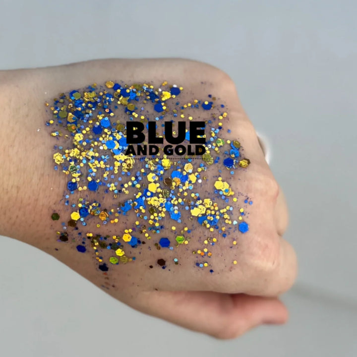 Photograph of cosmetic glitter on the back of a hand featuring blue and gold hexagonal flakes with a bold black text overlay reading BLUE AND GOLD
