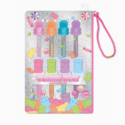 Product photograph of a Gummy Bear themed stationery set featuring four translucent bear-topped pens and sticky note flags against a silver glitter background with colorful candy illustrations and a pink braided strap