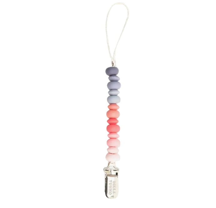 Silicone and metal pacifier clip by Bella Tunno featuring a vertical ombre gradient of flat oval beads in shades of grey, light blue, and warm coral centered on a white background with a silver-toned metal clip and white nylon cord loop