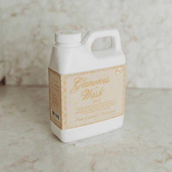 Photograph of a Tyler Candle Co white plastic jug of Diva scent Glamorous Wash laundry detergent on a marble countertop featuring the high-efficiency he logo and elegant gold script on a cream-colored vintage label