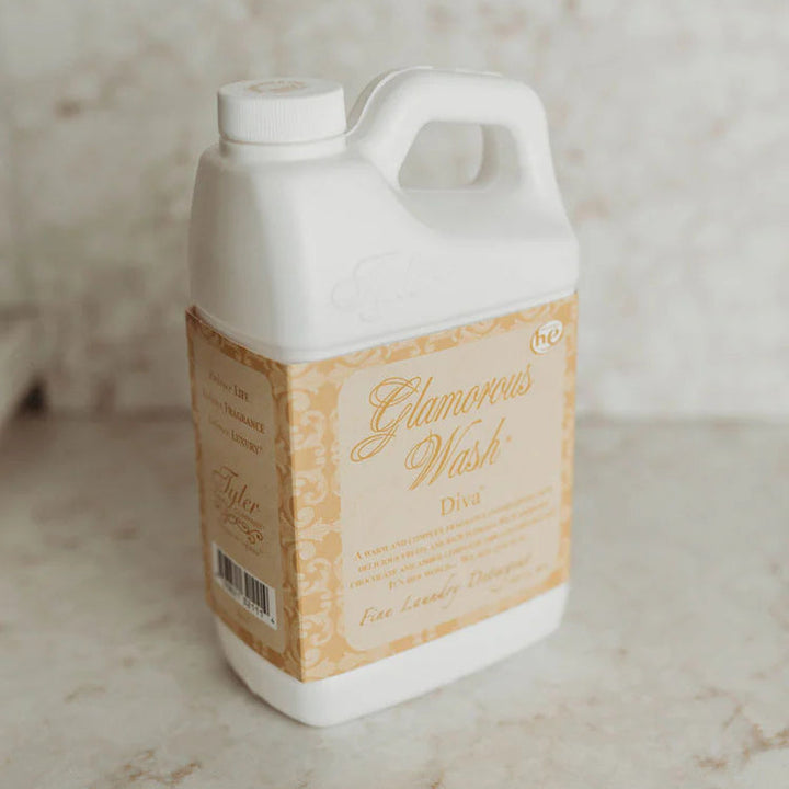 Product photograph by Tyler Candle Company of a white jug of Glamorous Wash Diva fine laundry detergent on a neutral marble surface featuring an ornate gold patterned label and elegant cursive typography