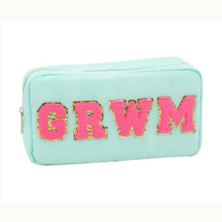 Nylon textile product photography of a mint green rectangular cosmetic bag featuring iconic pink chenille varsity letters spelling GRWM with shimmering gold glitter outlines and a top gold zipper against a clean white background