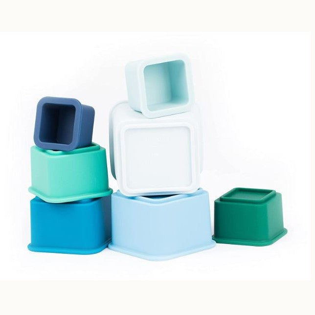Digital photograph of square silicone nesting cups in shades of teal, navy, and white arranged on a plain white background with smooth matte finishes and soft rounded edges