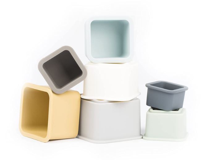 Product photograph of square silicone baby nesting cups arranged on a plain white background featuring a palette of muted mustard yellow, dusty blue, and neutral grey with soft rounded edges