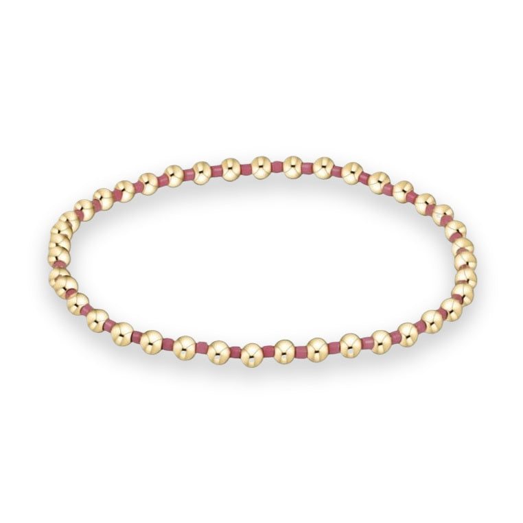 Gold-tone and enamel jewelry featuring a beaded stretch bracelet with polished spherical beads and matte mauve spacers arranged in a loop on a white background
