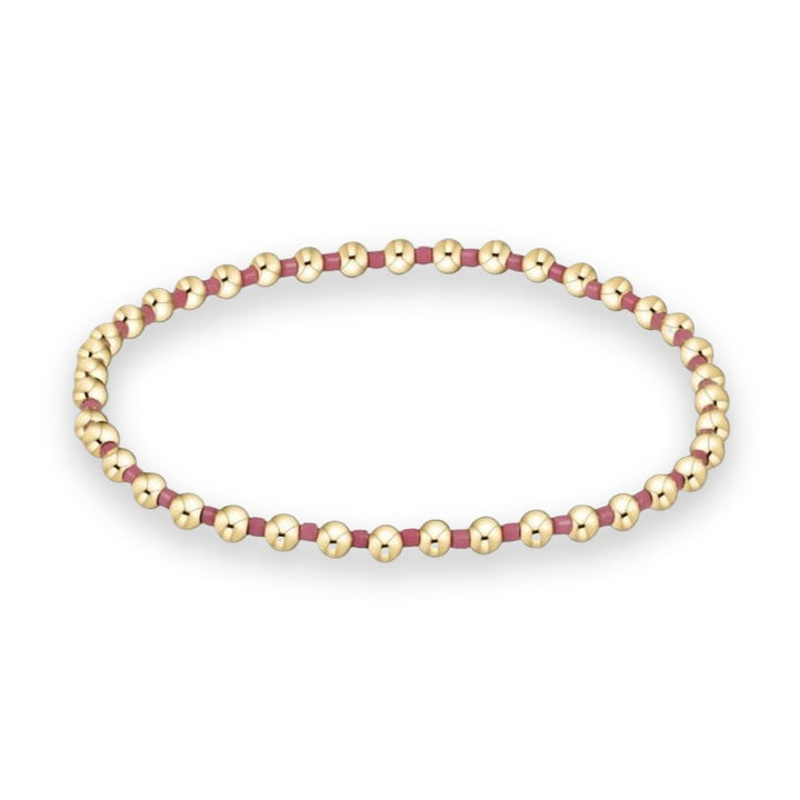 Gold-tone and enamel jewelry featuring a beaded stretch bracelet with polished spherical beads and matte mauve spacers arranged in a loop on a white background