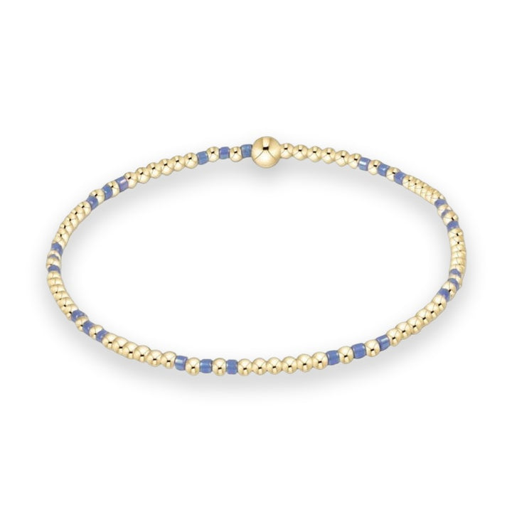 Handcrafted beaded jewelry featuring a delicate gold stretch bracelet on a white studio background designed with alternating polished gold spheres and iridescent periwinkle blue spacers and a single large gold bead focal point