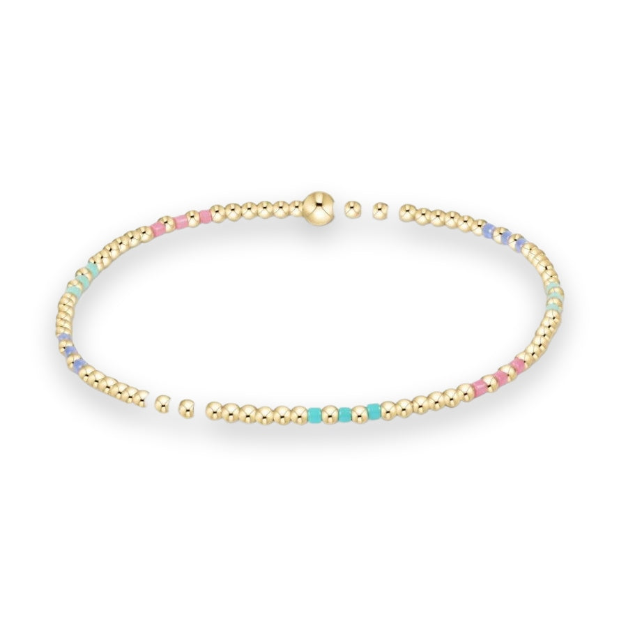 Beaded jewelry featuring a polished gold-tone stretch bracelet with round beads and colorful pastel pink, turquoise, and lavender enamel cylinders on a neutral white background