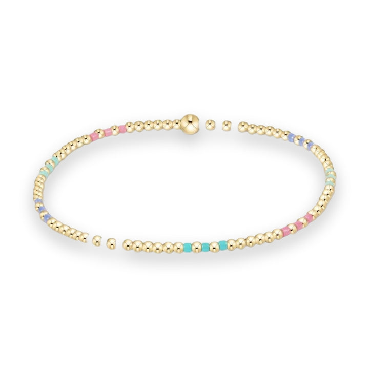 Beaded jewelry featuring a polished gold-tone stretch bracelet with round beads and colorful pastel pink, turquoise, and lavender enamel cylinders on a neutral white background