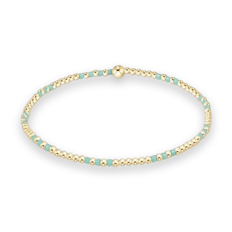Beaded gold jewelry bracelet presented on a white background featuring small spherical gold beads and mint green cylindrical accents with a single larger central gold bead